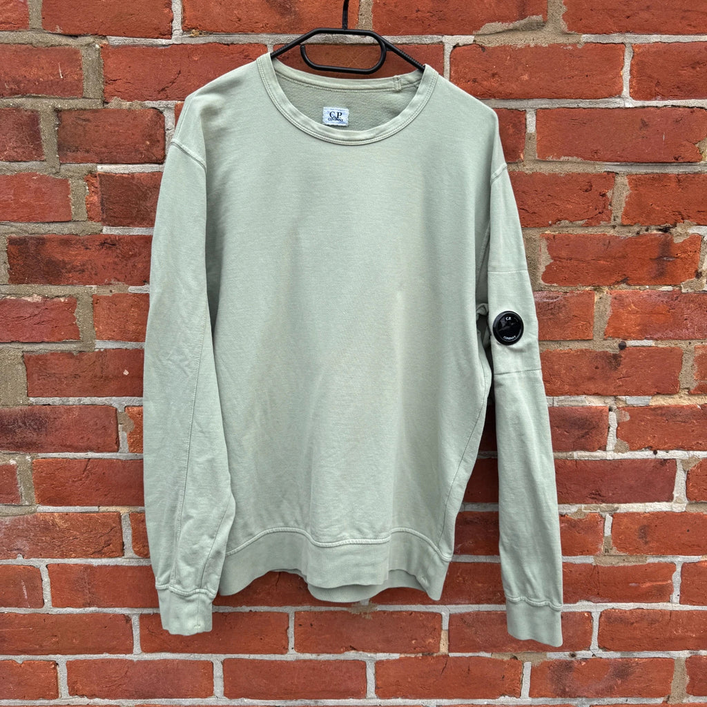C.P. Company green sweatshirt with ribbed hem and signature goggle lens detail.