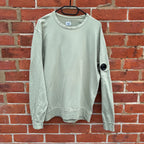 C.P. Company green sweatshirt with ribbed hem and signature goggle lens detail.