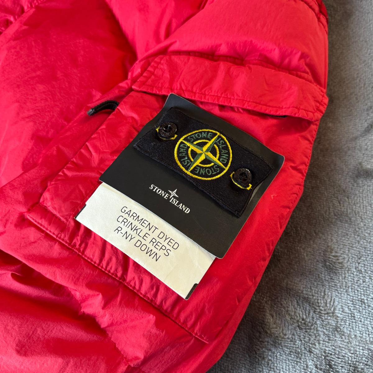 Stone Island red puffer jacket with compass patch, adjustable hood, and multiple pockets.