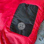 Stone Island red puffer jacket with compass patch, adjustable hood, and multiple pockets.