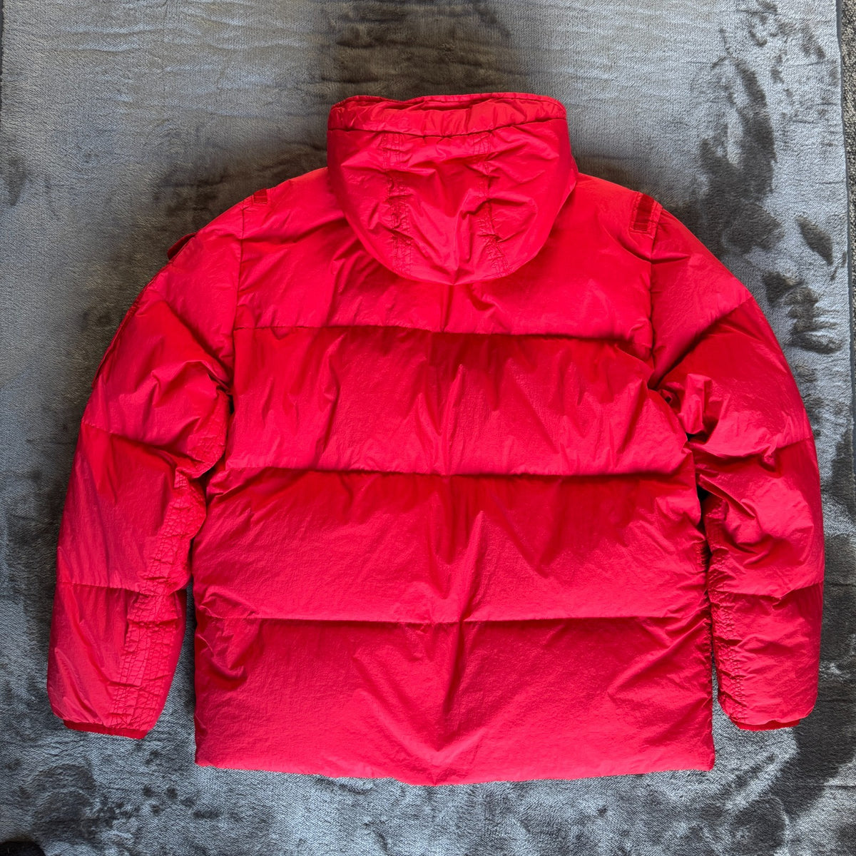Stone Island red puffer jacket with compass patch, adjustable hood, and multiple pockets.