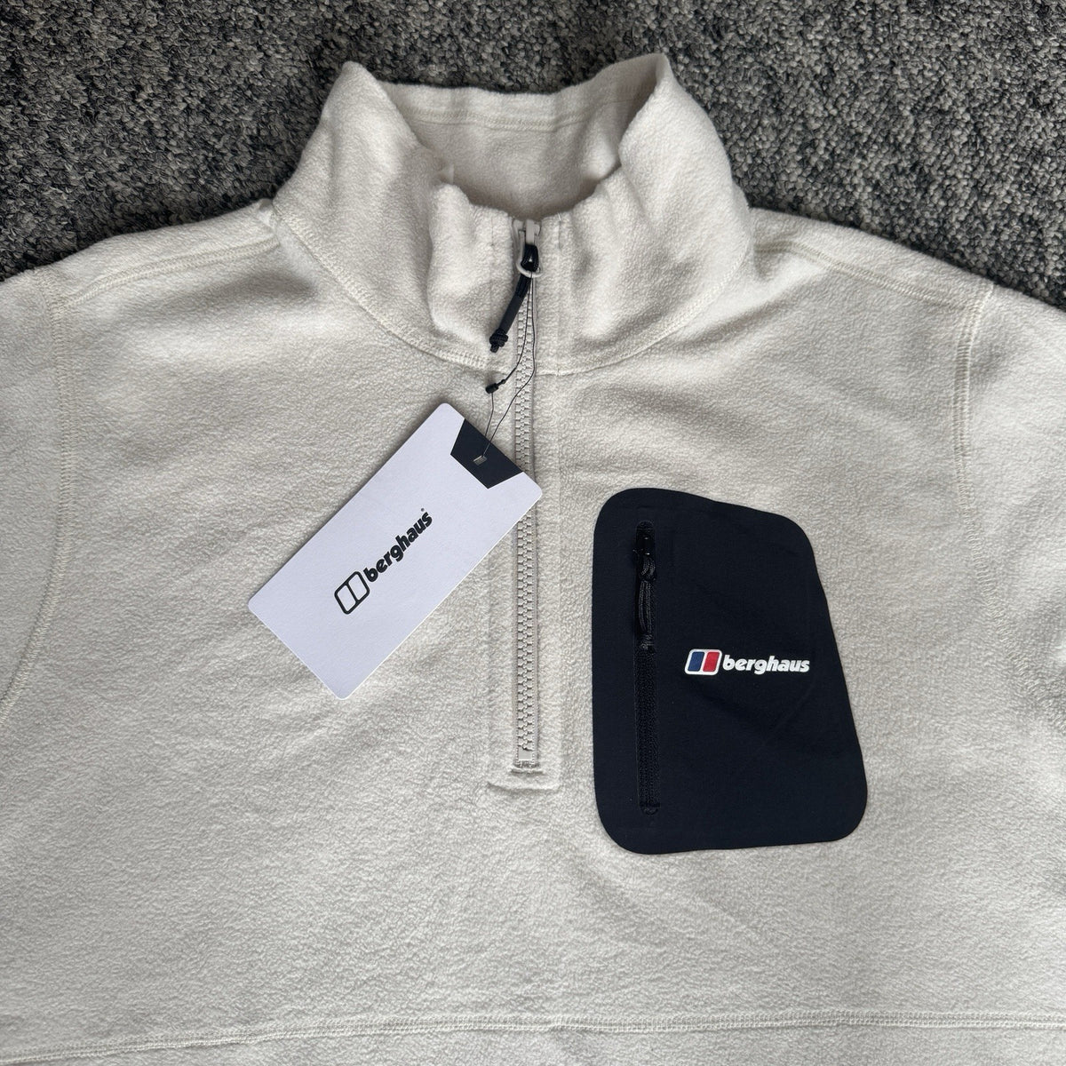 Berghaus off-white half-zip fleece with black logo pocket and stand-up collar.